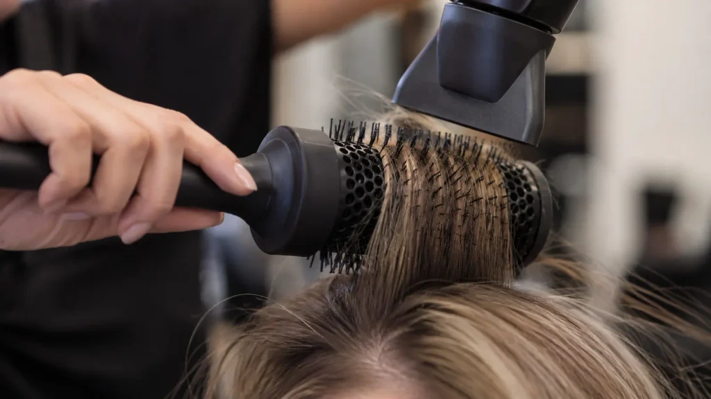 Asciugare i capelli senza volume con phon e spazzola rotonda vicino alle radici per sollevare i capelli fini e piatti, creare volume alla radice e ottenere una piega più corposa e leggera senza appesantire la chioma.