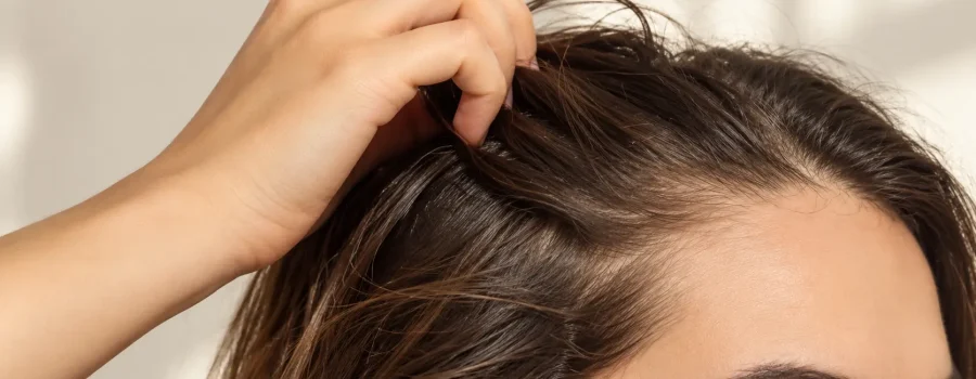 Donna con capelli fini e senza volume che solleva le radici con le dita per mostrare la cute, esempio di capelli piatti e consigli per ottenere maggiore volume e corpo con una corretta routine di detersione e styling.