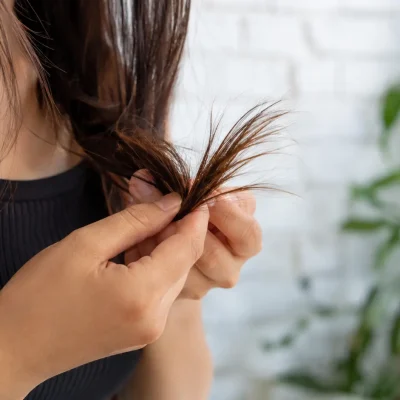 Donna osserva e separa le punte dei capelli lunghi castani per valutarne la porosità, la struttura della fibra capillare e lo stato delle lunghezze, concetto di capelli porosi, cuticole dei capelli, capelli secchi, crespi e trattati, analisi della porosità dei capelli e cura cosmetica delle lunghezze.