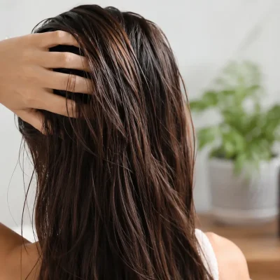 Donna con capelli grassi che controlla la cute davanti allo specchio in un bagno luminoso, immagine rappresentativa della corretta frequenza di lavaggio dei capelli grassi.