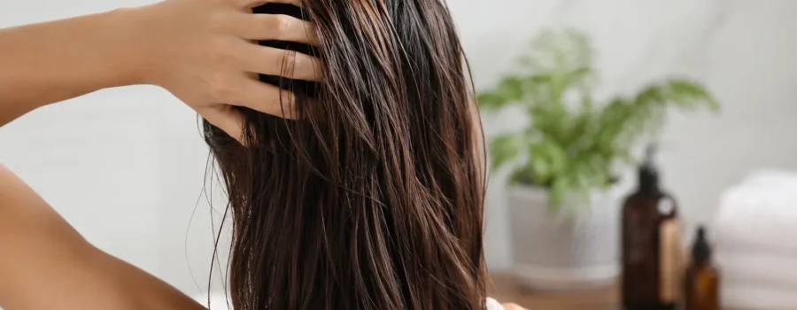 Donna con capelli grassi che controlla la cute davanti allo specchio in un bagno luminoso, immagine rappresentativa della corretta frequenza di lavaggio dei capelli grassi.